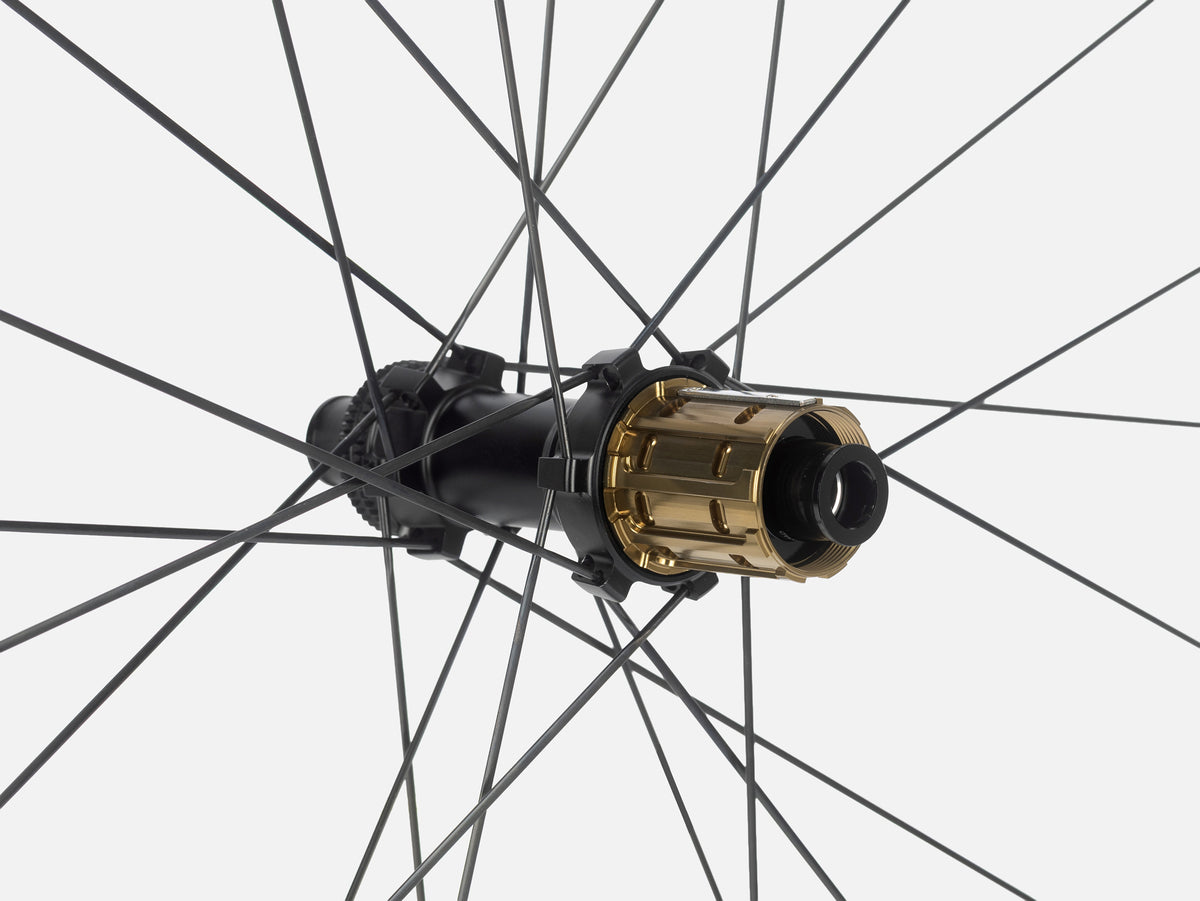Close-up of Litebike Arc-35 carbon bicycle wheelset hub with a gold-colored outer cover and black inner components, surrounded by thin black spokes against a light gray background.